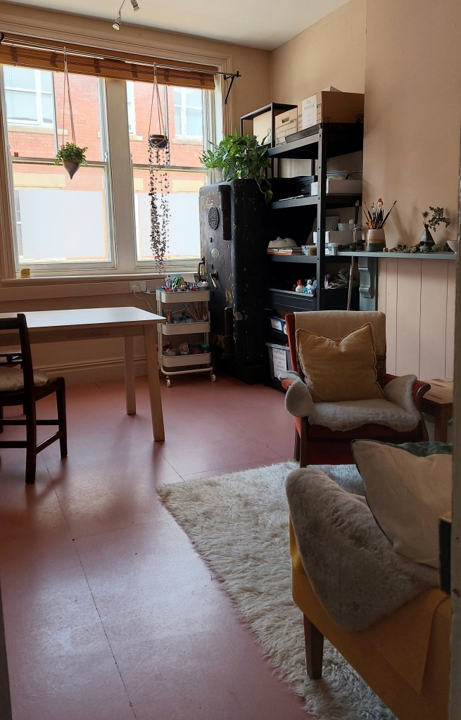 A calm, inviting art therapy room with comfortable chairs arranged for conversation and shelves of art materials.
